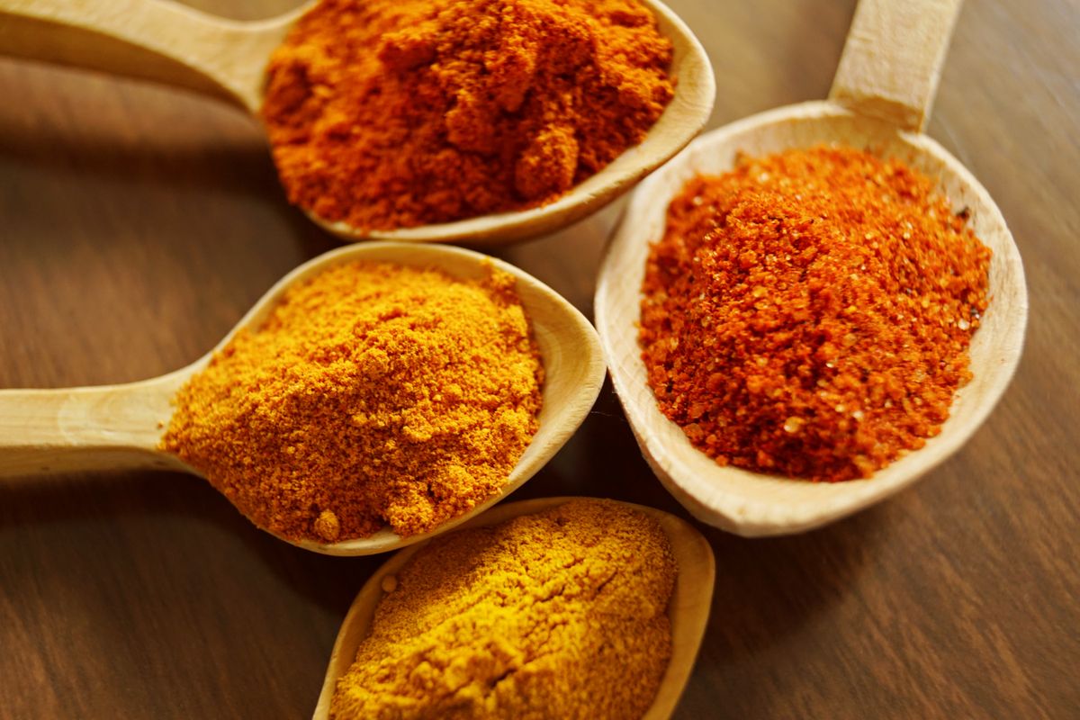 Wooden spoons holding turmeric, chili, and masala powders